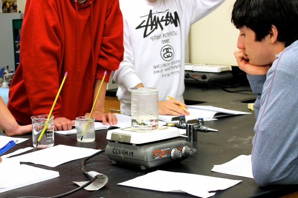Chemistry students gather around a beaker during an in-class lab.   Photo by Levi Schoeben.