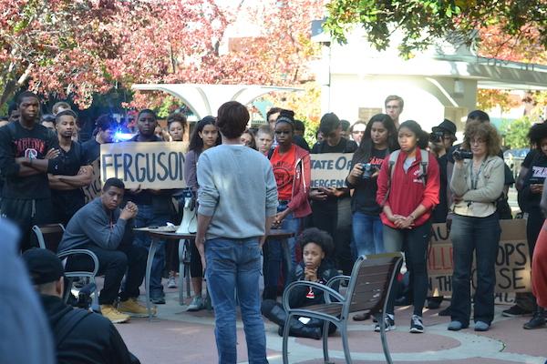A crowd of peaceful protesters listens to one protestor as he talks about the brutality of racism. Police lights shine in the background as the Palo Alto Police Department blocks off the street for the protest. Photo by Amy Leung.