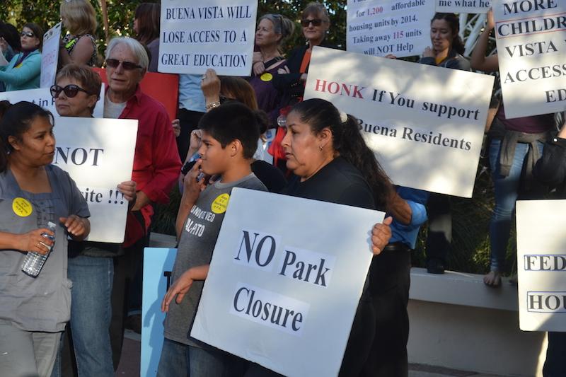 A woman and boy hold signs alongside about 50 others to protest the closure of Buena Vista Mobile Homes in front of Palo Alto City Hall. Photo by Amy Leung.