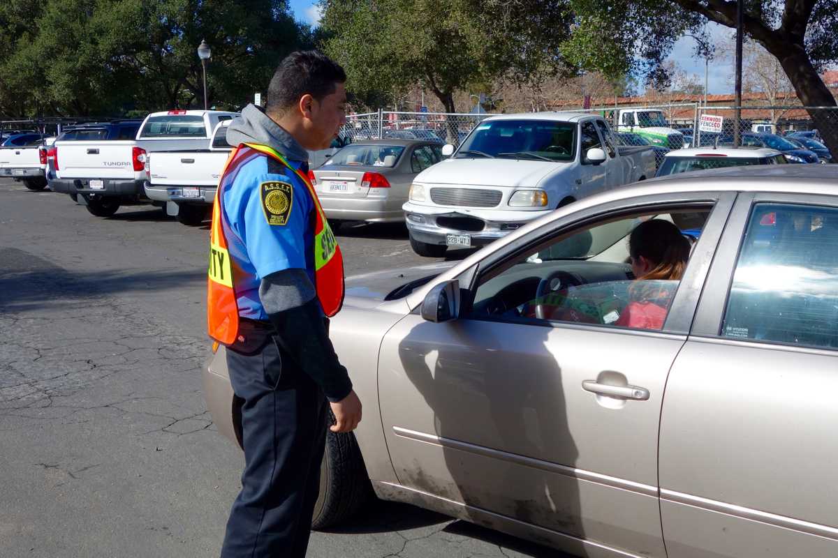 A hired security officer examines a student's parking permit. The Paly administration has upped security measures in light of Super Bowl 50 traffic.