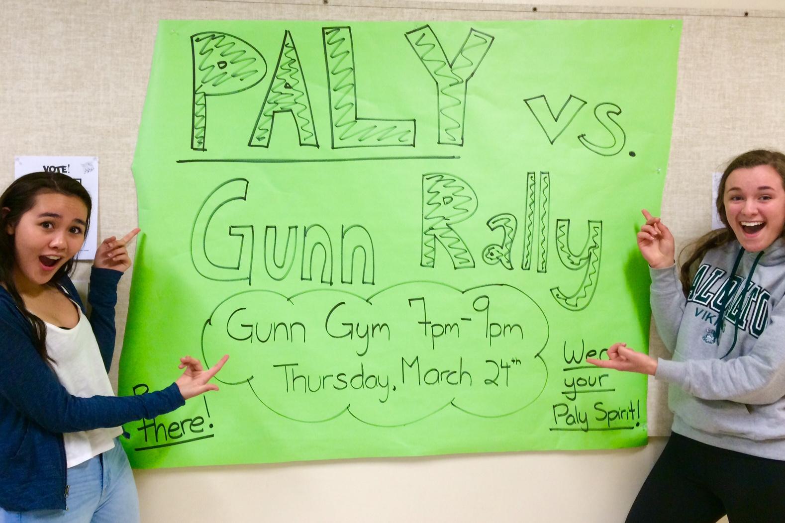 Juniors Kaitlyn Vi and Nora Danie stand in front of the promotional poster for the upcoming night rally.