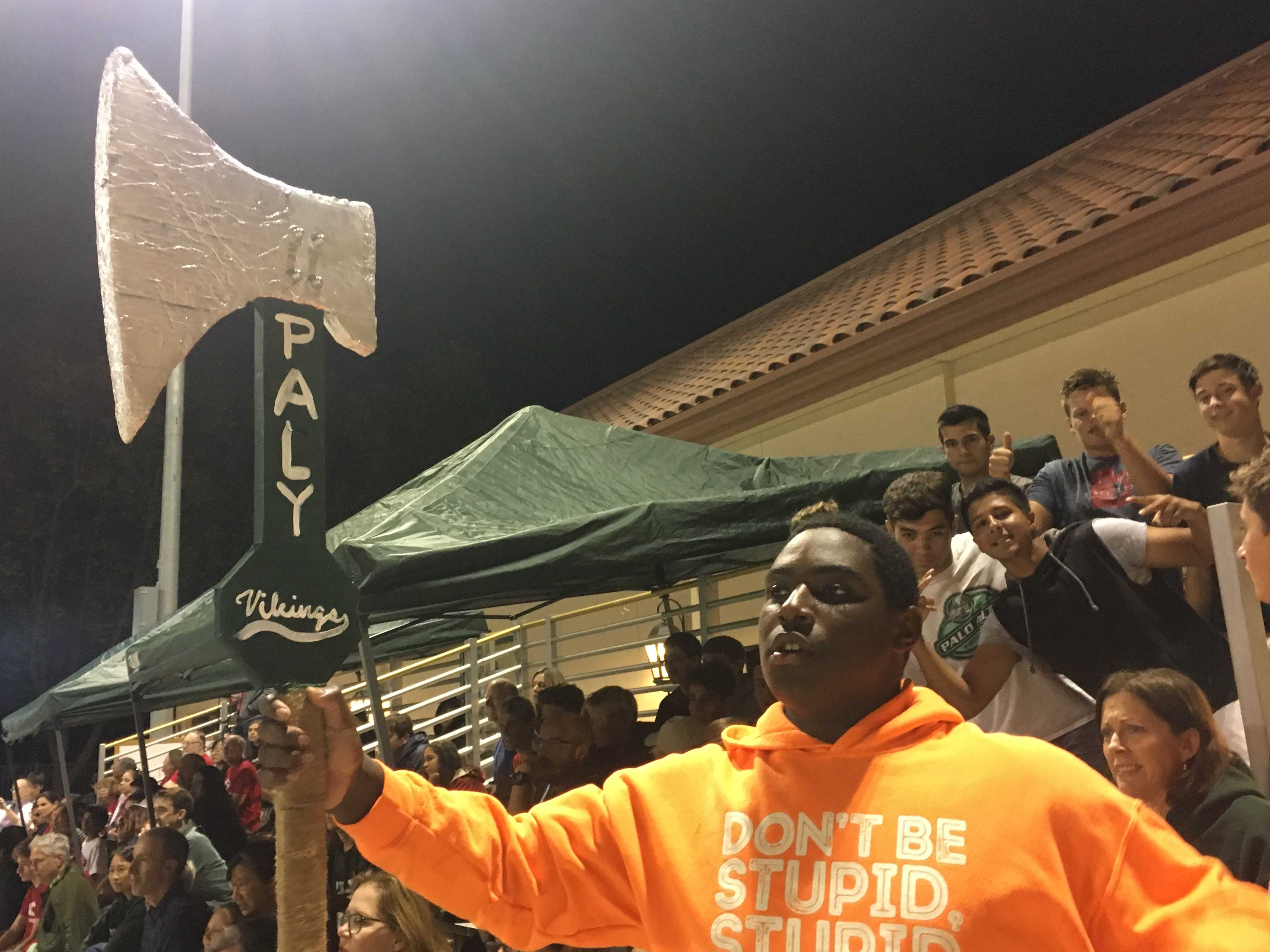 Junior Alex Daw raises an axe to cheer for the team, and other students in the stands support him energetically. Photo: Soumya Jhaveri