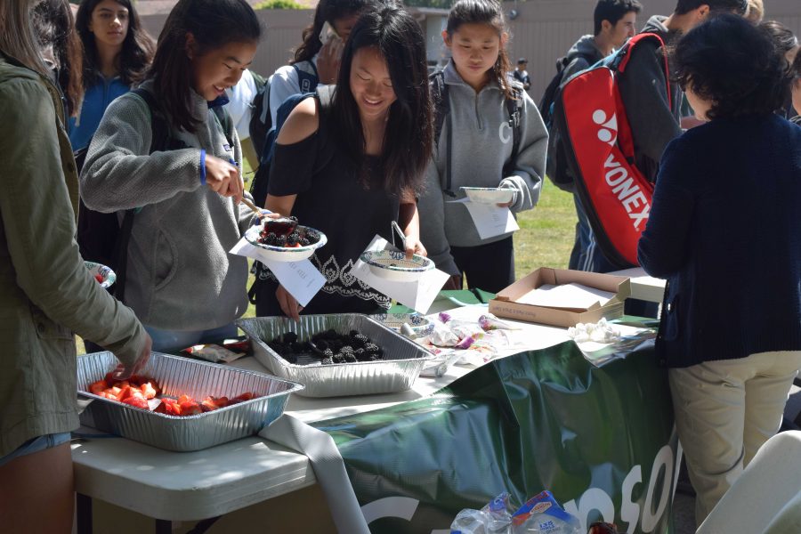 Sophomore Samantha Kao, left, grabs a healthy snack. Parent volunteers served locally grown fruit and granola during Day 1 of Change in Our Schools week,    which focuses on issues that need change at Palo Alto High School. “Change in Our Schools Week is something that the School Wellness and Climate Committee has been working on that is basically a whole week long full of events during lunch time that focus on changes in our school, like bringing more awareness to certain events or certain things that we would like to focus on more as a school, junior Noor Navaid said.