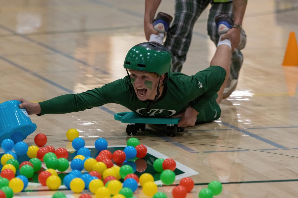Senior Asher Friedman skids across the gym floor while playing Hungry Hungry Hippos in a rally last fall in the Peery Center Gym at Palo Alto High School. This year, as a result of a volleyball lodged in the bleachers, rallies in the gym have been moved outdoors. According to girls volleyball coach Chris Crader, the ball  is preventing the bleachers from expanding, making one side of the gym unusable to seat students. “Once the bleachers get sideways, they don’t go in or out,” Crader said. (Photo: Daniel Garepis-Holland)
