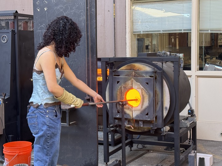 Sophomore Stella Guo holds a piece of glass in the furnace to heat up her new project. According to Guo, she suggests eighth graders interested in taking the course to do preview research before getting their hands straight into glass blowing. “Start by watching for two months and then start doing it, because if you don't do that it's really dangerous,” Guo said. “Glass blowing can be really intimidating, but as long as you watch and watch our teacher do it for a few times and you start doing it to be a lot better.”