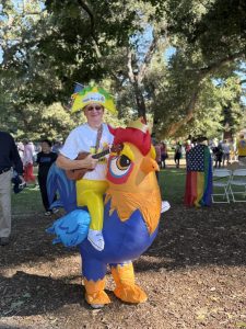 A protester in a chicken suit wearing a taco hat with the words “Cluck Trump” at the “No Kings” Democracy Fair in Palo Alto on Saturday. Protestor Mary Chan said she and her husband are horrified at the state of science and medicine in America. “What he [Trump] is doing by defunding scientific research is destroying our academic medical centers, and he’s [Trump] bankrupting rural medical centers,” Chan said. “We will have lasting negative impacts on American health for decades.”