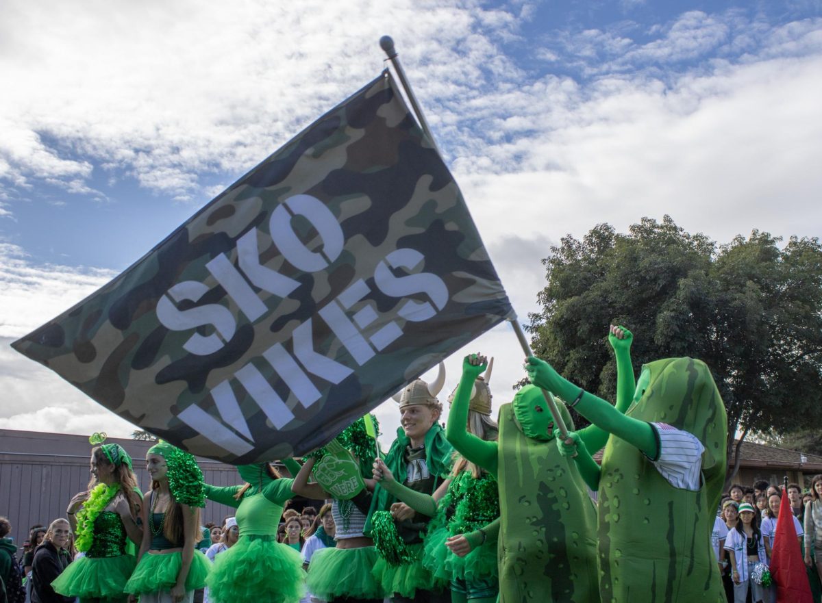 Senior Sarah Thieman waves the senior flag while awaiting the decision for the best-dressed competition at brunch on the Quad. Thieman said her inspiration for the costume was her love for pickles. “We love pickles, and they’re green,” Thieman said. “Like what else would be better?”