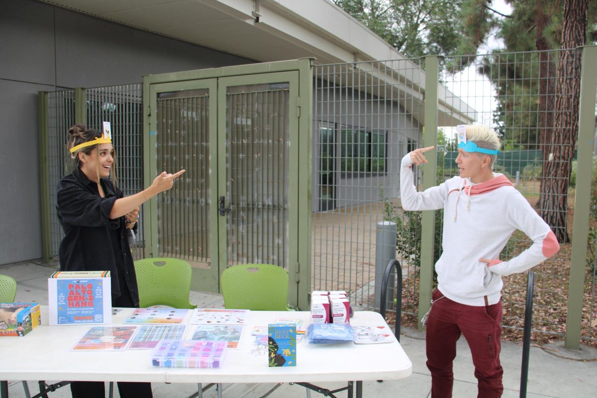Allcove therapist Reyna Kurain (left) and Tessa Reynolds (right), a rehabilitation counselor at The Q Corner, play a game of Guess Who on Oct. 1 while waiting for teens to check in for Gen Z Hang at Mitchell Park. They provided access to mental health support for teens at the gathering. In an email to The Paly Voice, The Q Corner Team stated that the Gen Z Hang event is one in a series of pilot events. “The planning team will evaluate whether to continue these gatherings beyond October 2025 based on community interest and feedback,” the email stated.