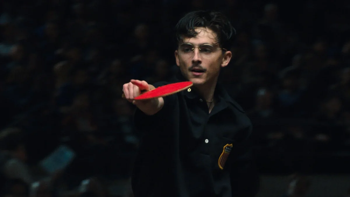 Marty Mauser (Timothée Chalamet) raises a paddle to his opponent at the British Open table tennis tournament in "Marty Supreme," which is nominated for nine Oscar awards — including Best Picture, Best Director and Best Leading Actor.