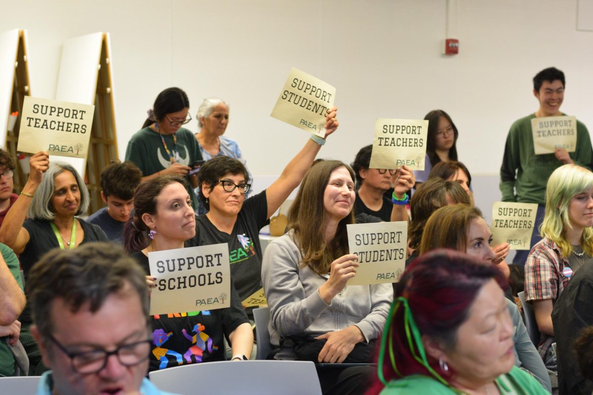 Board member attendees hold 'support students,' 'support teachers' and 'support schools' signs in a full room at 6:30 p.m. today. According to Palo Alto Educators Association president Tom Culbertson, weakening communication between staff and district leadership has led to worsening morale and added strain on educators’ well-being. "We [PAEA] have seen an erosion of collaboration [and] professional trust, and that manifests it low morale and difficulties with mental health."