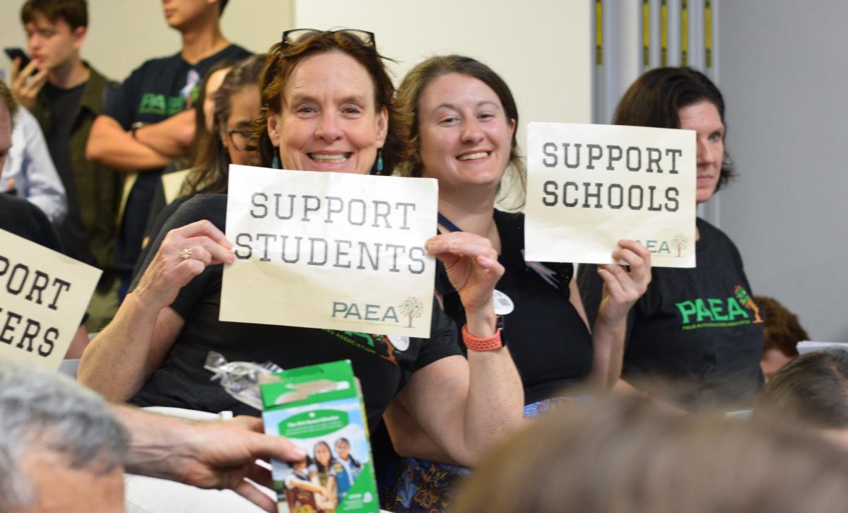 AP Capstone teacher Lucy Filppu and computer science teacher Kathryn Widen hold signs and chant for the board meeting to begin.