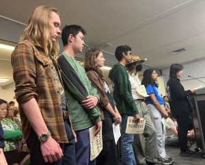 A group of students line up to deliver a "continuous speech" at the March 17 Palo Alto Unified School District school board meeting. According to junior Dorian Luo (speaking), both the students and administration want to connect with each other. “Students need to see the changes being made,” Luo said. “We know you are all working so hard behind the scenes. Please, help us bring your work to the public’s attention.”