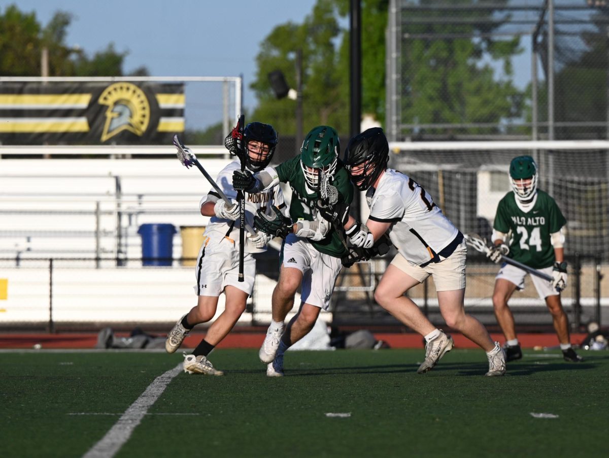 Viking freshman Quentin Studdert squeezes past two Trojan defenders Thursday night at Mountain View High School. According to Viking junior Richie Zhang, the Vikings had a solid performance overall. "We could definitely work on just our passing, catching, and just our sloppiness," Zhang said. "But we did well pretty much everywhere else, like our goalie, face off, everything was clicking."