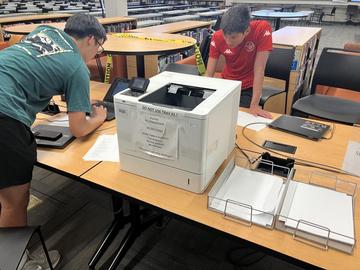 Two students use the library printer to print their next assignment. According to English teacher Sarah Bartlett, students learn better when using paper. “Most kids do better with paper handouts.” Bartlett said. You can write on it, you can find it, you can physically put your hands on it, you can have three handouts out on your desk at once, versus searching through Schoology and splitting the screen.”
